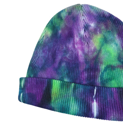 Tie-dye knit beanie hat showing curved crown and ribbed purple-green cuff